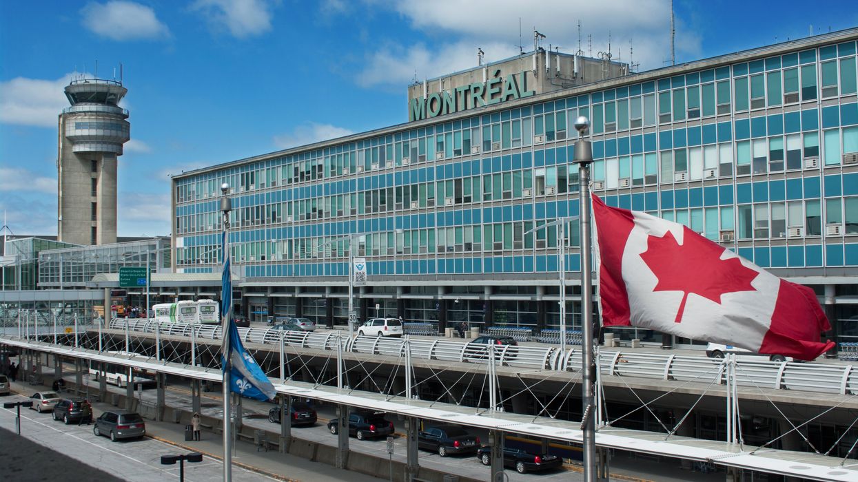 The exterior of Montréal-Pierre Elliott Trudeau International Airport with a Canadian flag blowing in the wind in front of it.