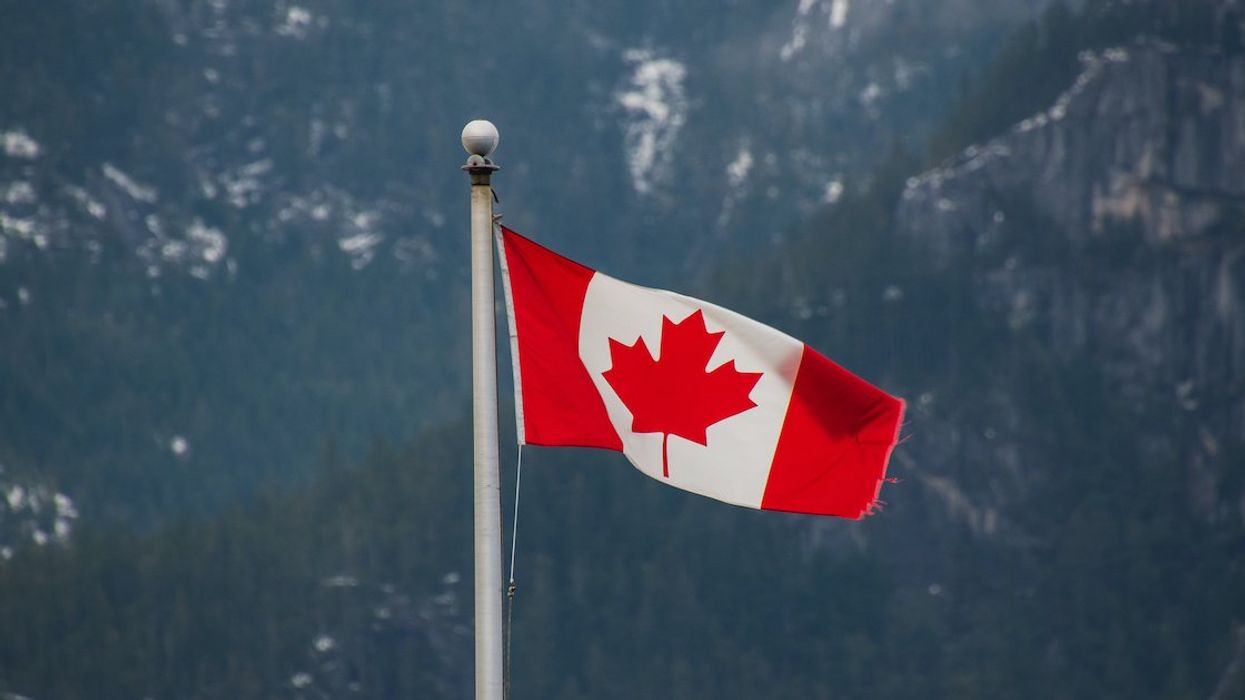 The flag of Canada against a backdrop of pine and snow-covered mountains.