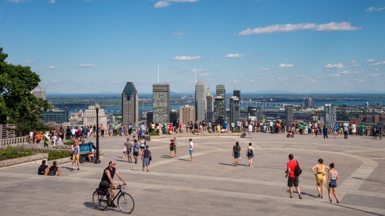 The Montreal skyline taken from the Mont-Royal lookout during the summertime with various people walking and biking around.