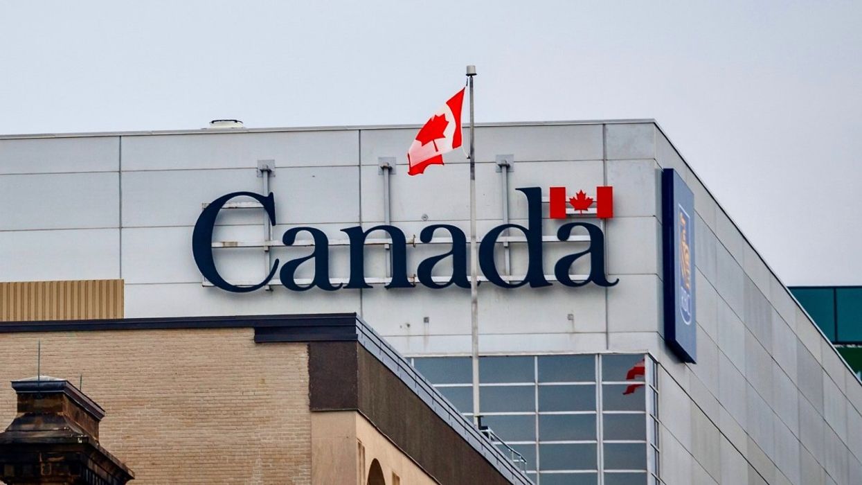 The official logo of the Canadian government, on an administrative building next to a Canadian flag waiving.