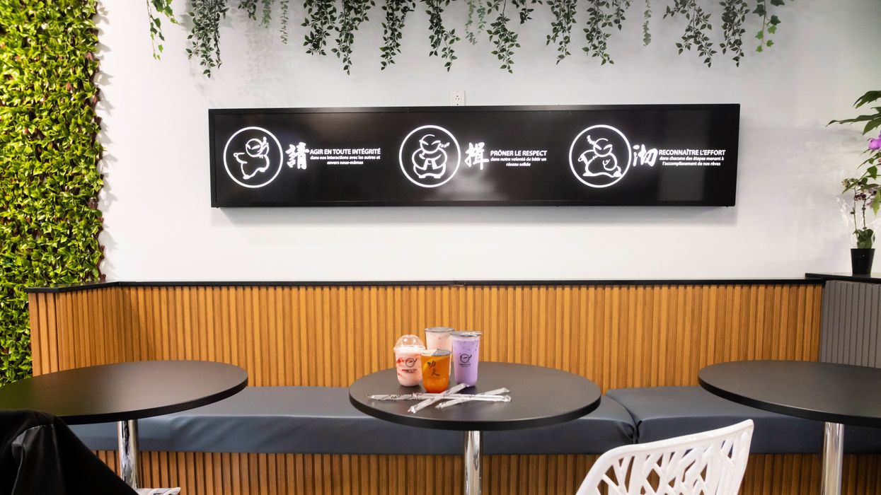 The strawberry yogurt slush, grapefruit green tea, rose green milk tea and taro milk tea on a table, below a sign with the Kung Fu Tea mascot and next to a green wall.