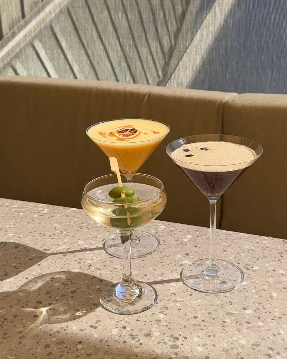 Three cocktails on a counter brightly lit by direct sunshine.