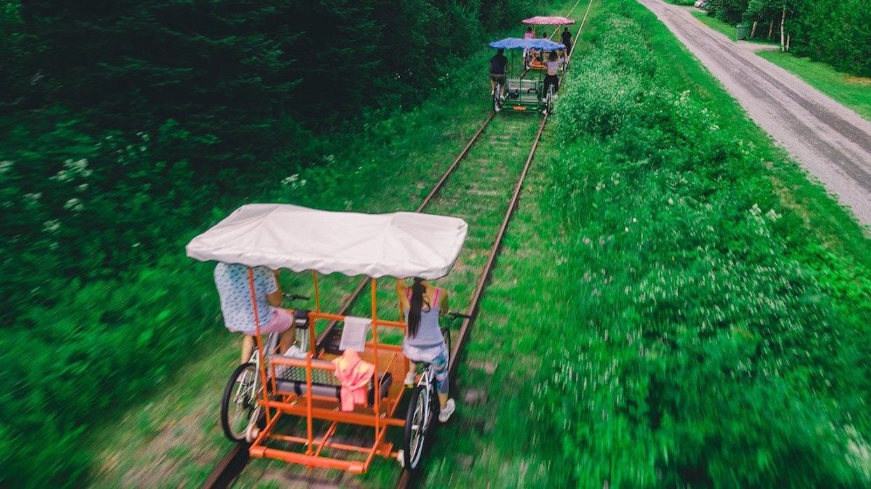 Three groups of people ride Vélorails bike carts on tracks along a dirt road.
