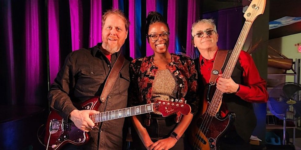 Three musicians posing for a photo; two of whom are holding guitars.