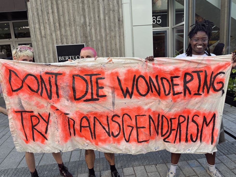 Three people hold a sign reading, "Don't die wondering, try transgenderism."