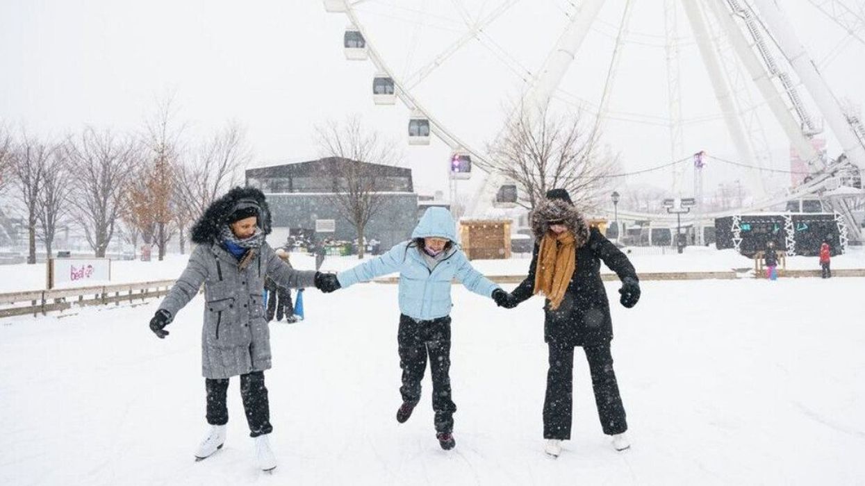 Three people skate on the ice rink in front of the Grande Roue.