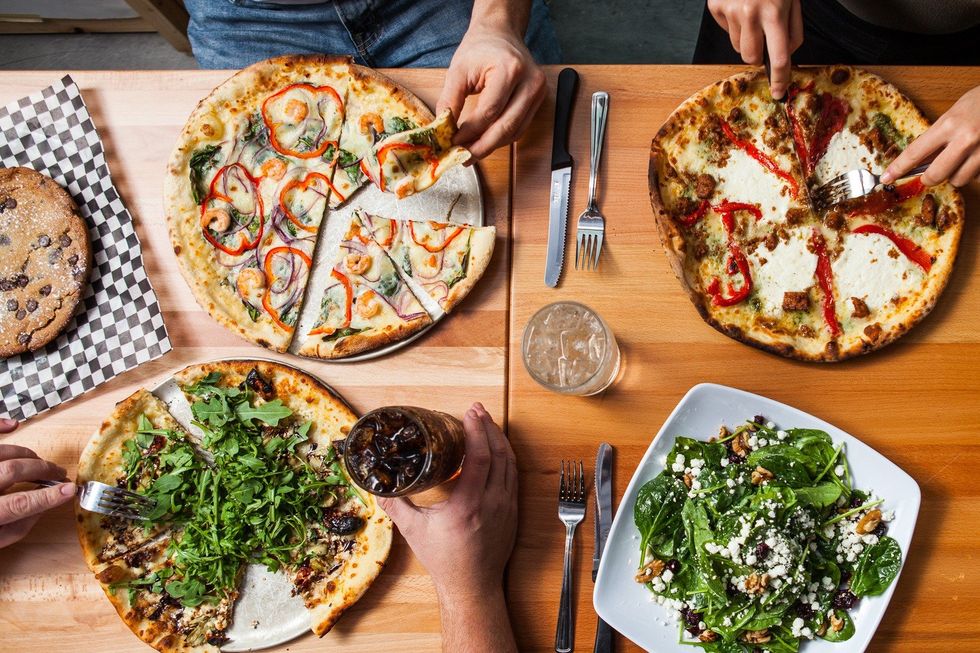 Three pizzas, a salad and a giant cookie arranged on a table.