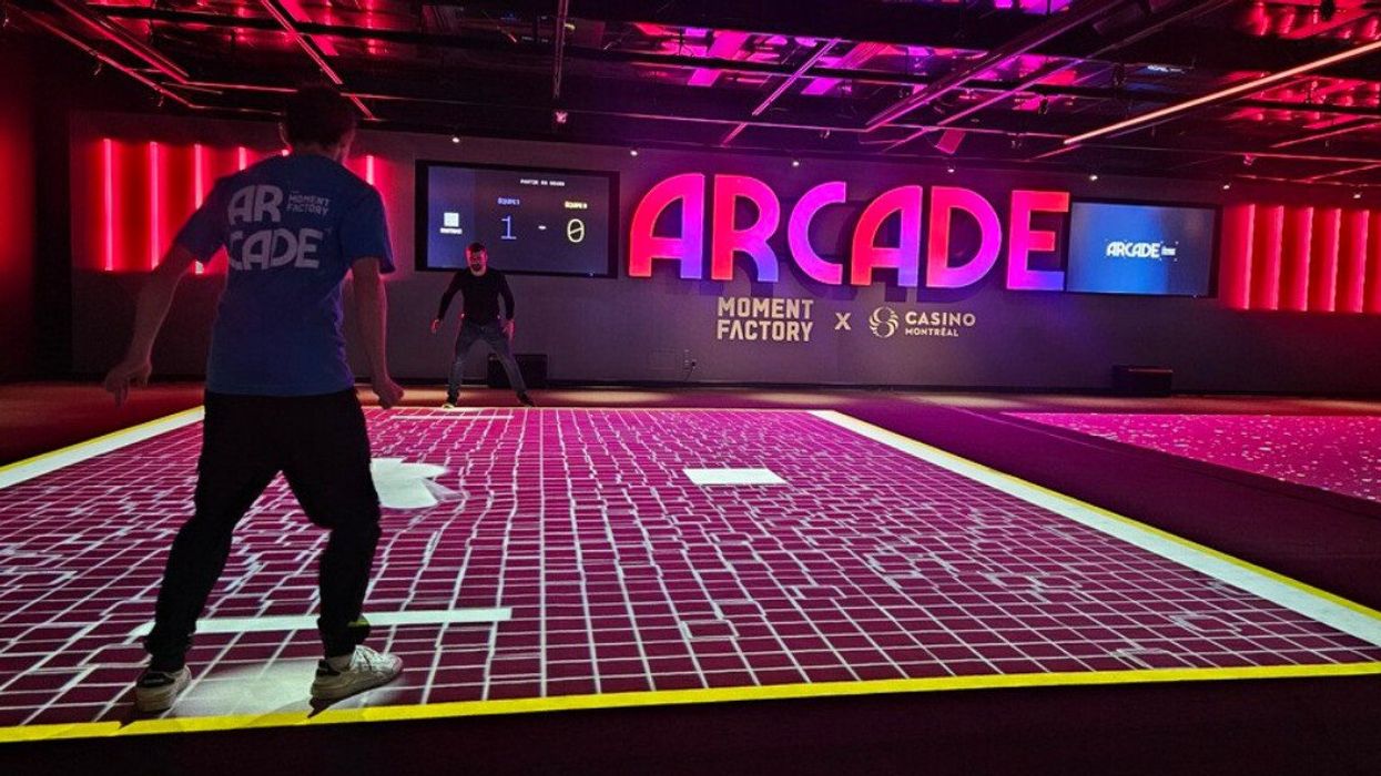 Two people on an illuminate floor-grid, part of a human-sized version of Pong, with "ARcade" in large neon letters on the wall behind.