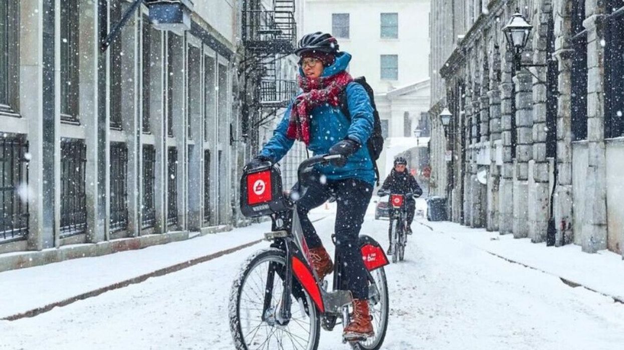 Two people riding BIXIs in a Montreal alley while it's snowing.