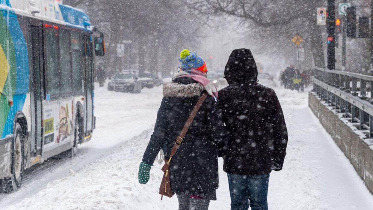 Two people walk on a snowy Monkland Avenue sidewalk.