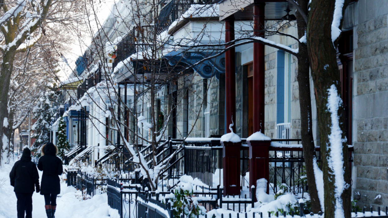 Two people walk on a street lined with Montreal homes during the winter.
