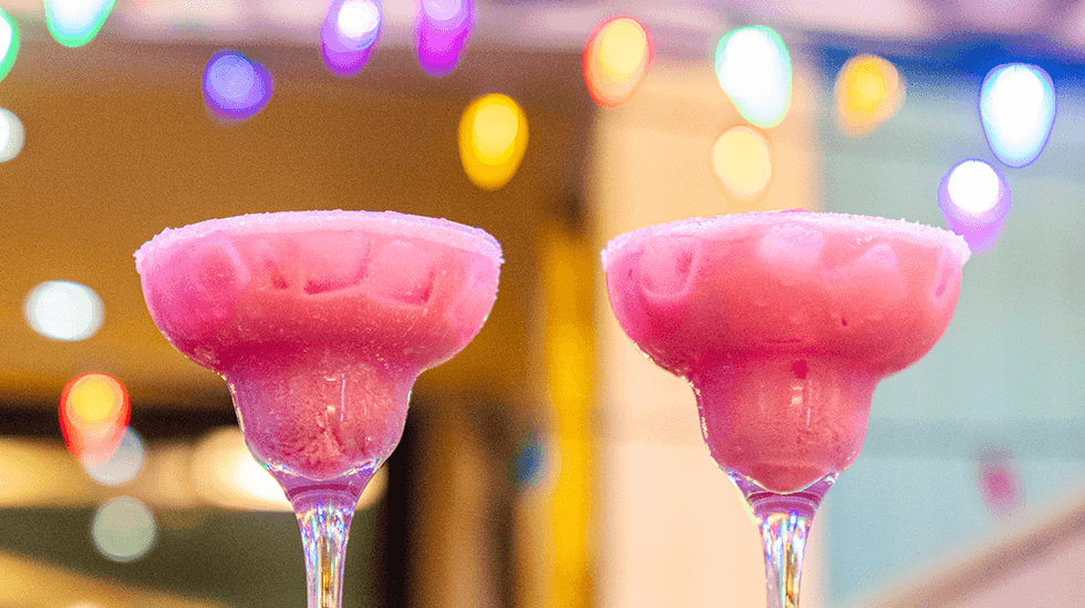 Two pink frozen cocktails in margarita glasses.
