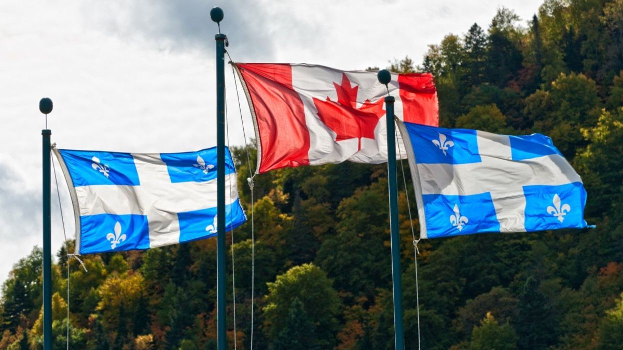 Two Quebec flag and one Canadian flag waving with trees in the background. 