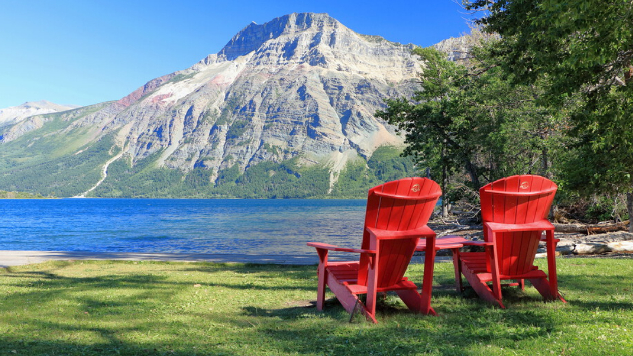 Two red Adirondack chairs sit in front of a lake at Waterton Lakes National Park.