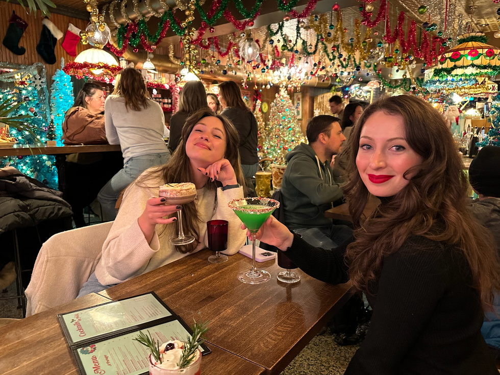 Two women smile while holding drinks inside La Taverne de Noel.