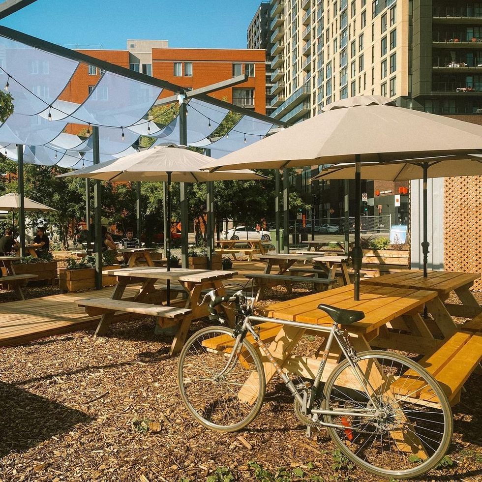 \u200bA bike leans against a picnic table under a blue fabric canopy with hanging lights.