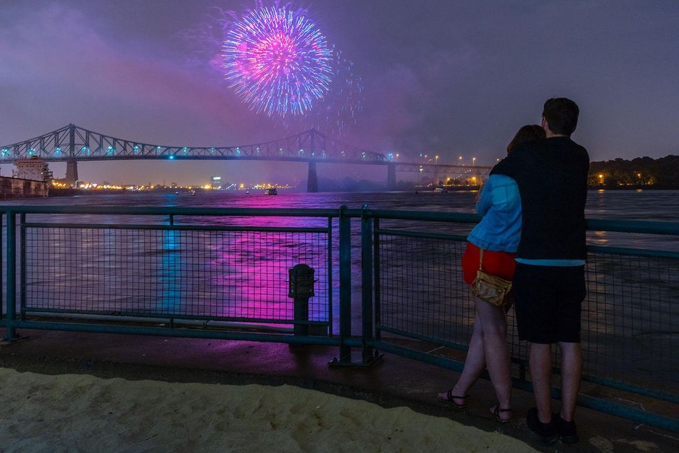 \u200bA couple hug each other next to the railing of the Clock Tower Beach watching a fireworks display over the water.