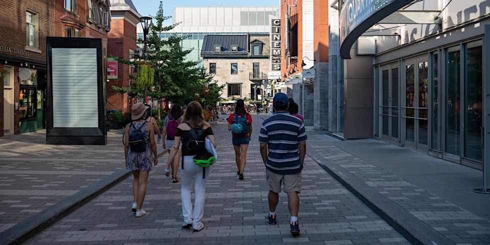 \u200bA group of people walking down a Montreal street during the summertime.