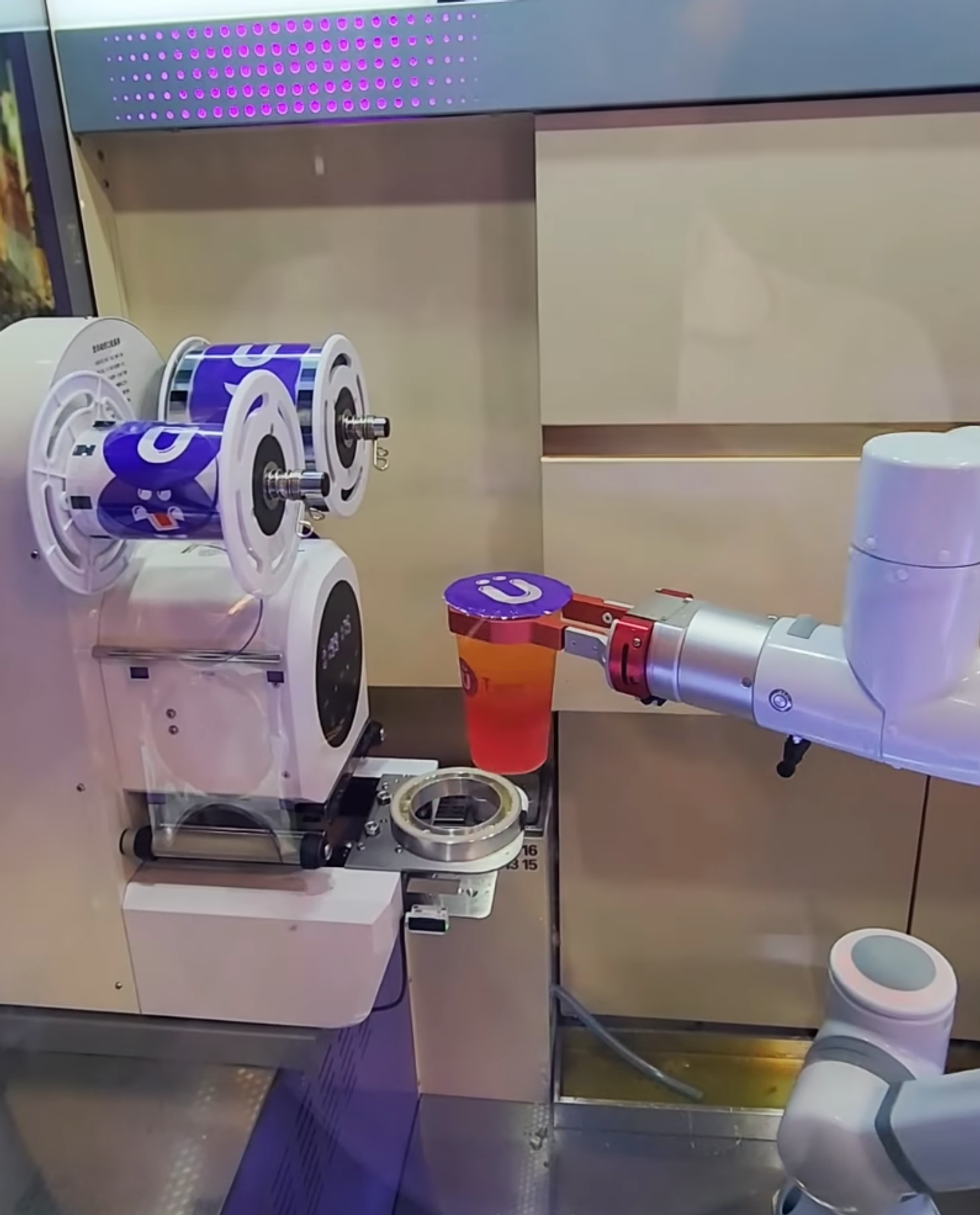 \u200bA robot arm holds a bright pink-orange bubble tea.