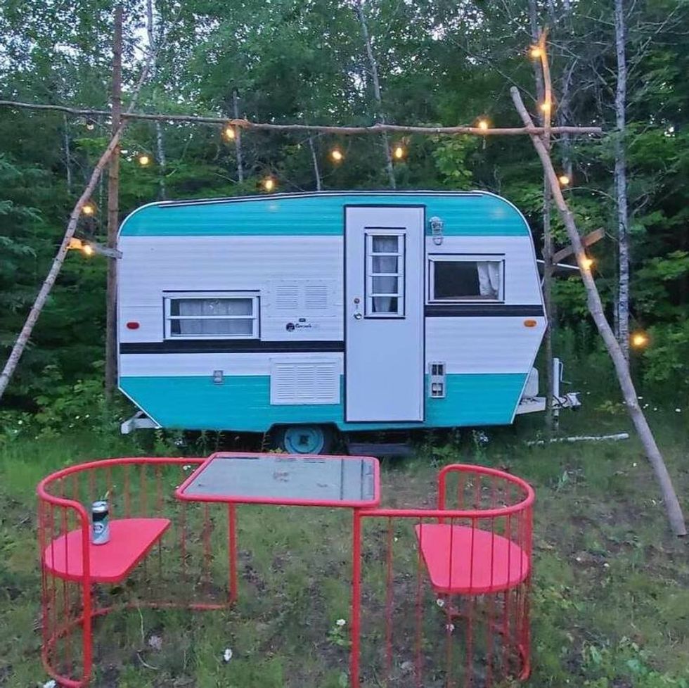 \u200bA teal and white camper van surrounded by fairy lights and a table and chairs our front.