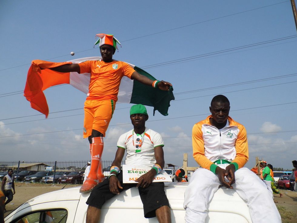 \u200bFootballs fans dressed in bright orange and white uniforms on a van in C\u00f4te d'Ivoire.