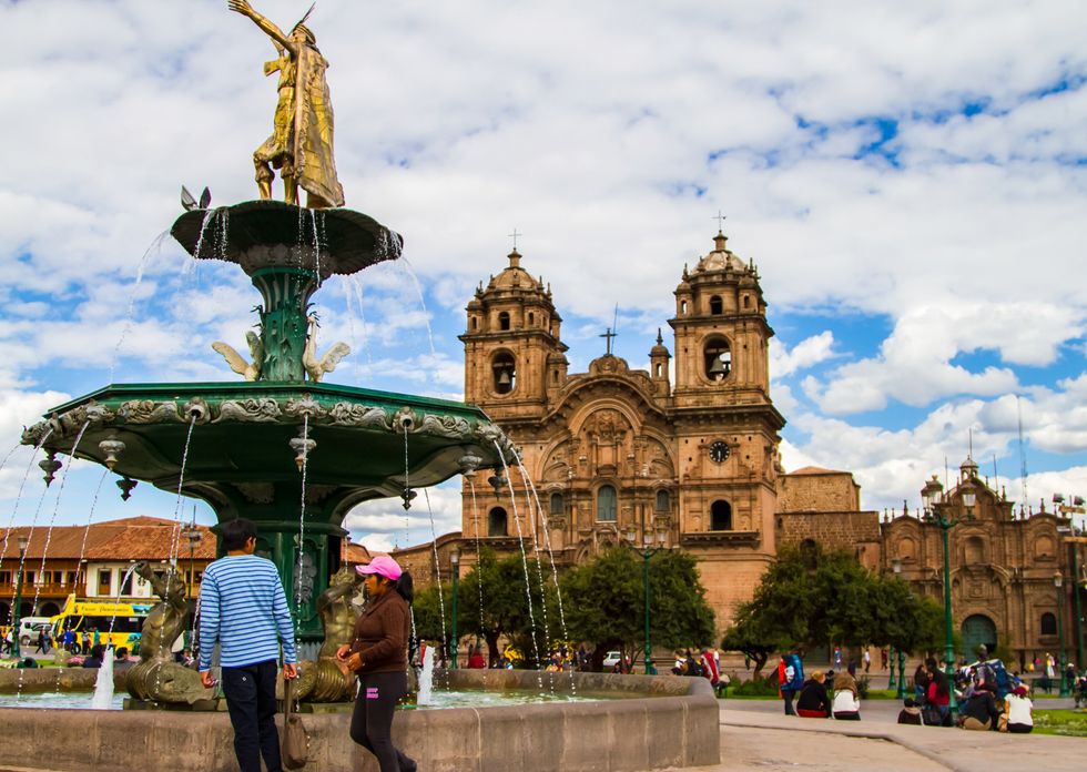\u200bPeople stand near a fountain in the main square in Cusco, Peru.