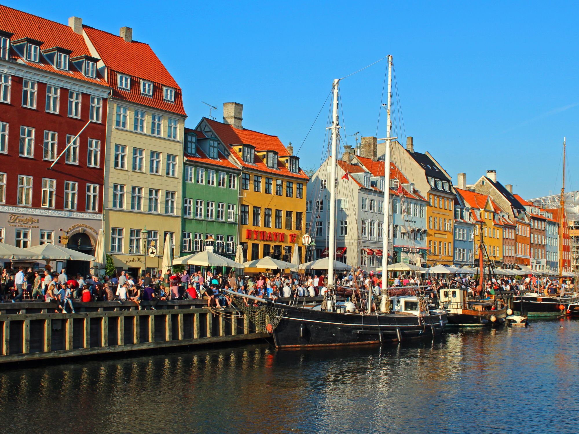 \u200bPeople walk by colorful houses on the Copenhagen waterfront in Denmark.