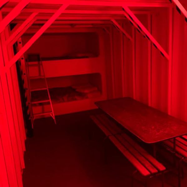 \u200bRed-lit bunkbeds by a table in the underground accommodation.