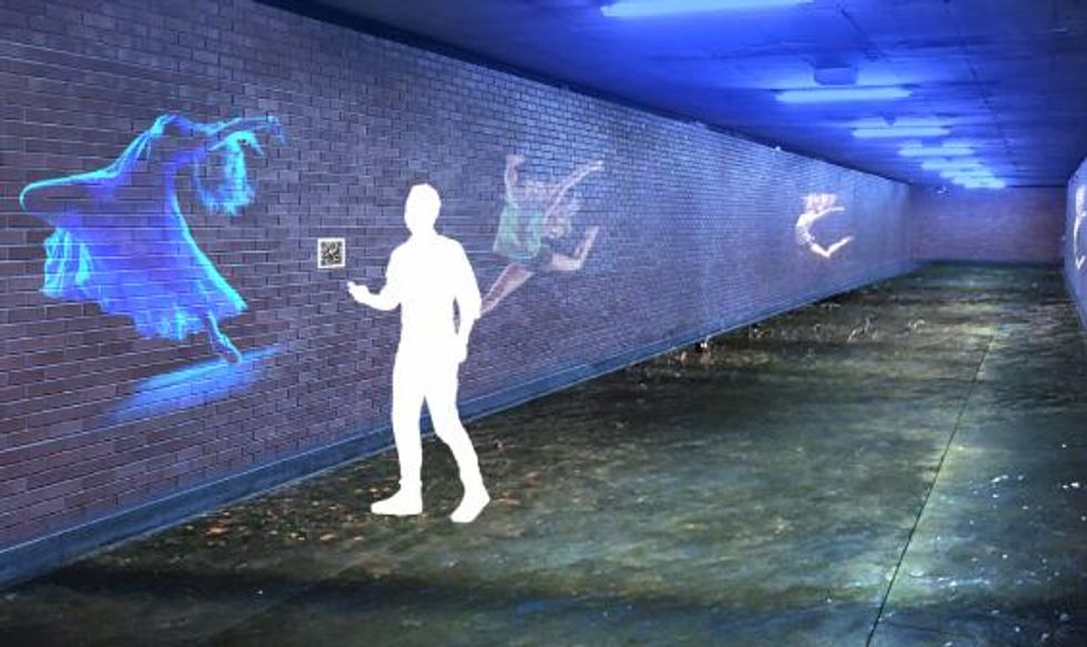 \u200bSomeone stands next to a projection of a dancer on a brick wall.