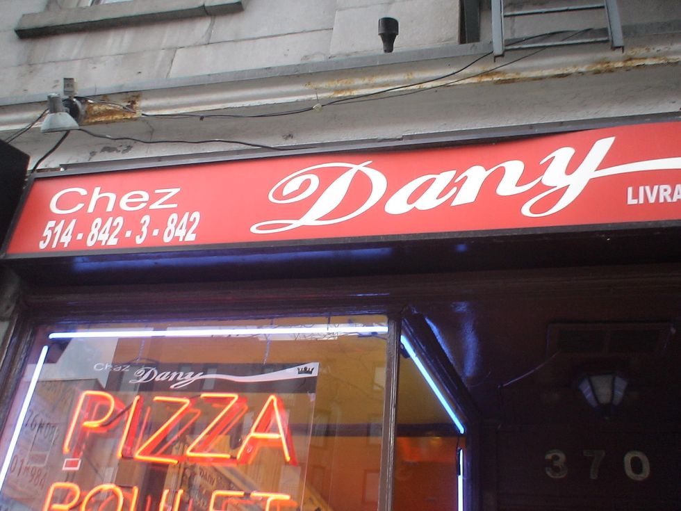\u200bThe entrance to Pizza Chez Dany with a neon sign in the window.
