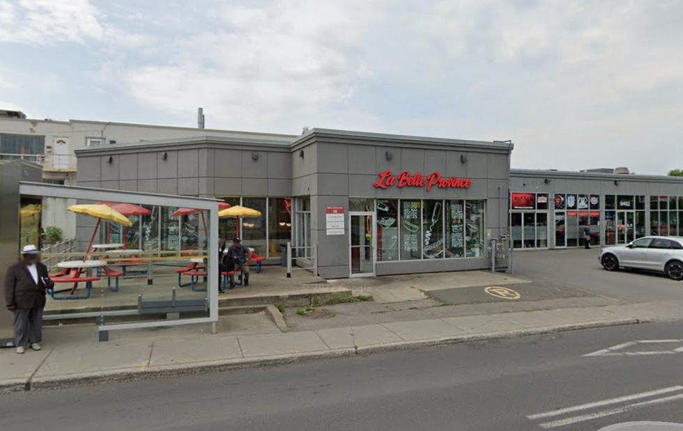 \u200bThe exterior of a La Belle Province fast food restaurant in Montreal located beside a bus stop and other stores.