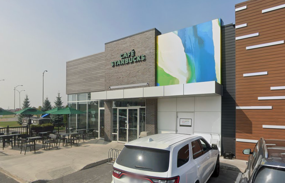 \u200bThe exterior of a Starbucks in Montreal with various cars parked in the parking lot and patio chairs and seating out in front.