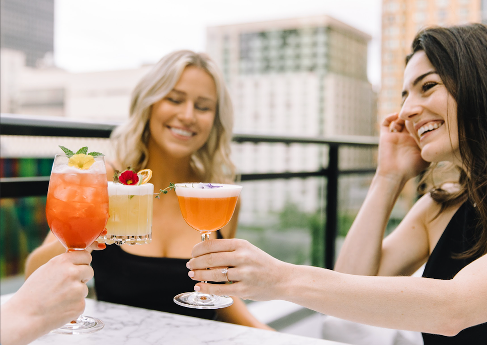 \u200bThree people hold drinks to "cheers" on the Aliz\u00e9 terrasse.