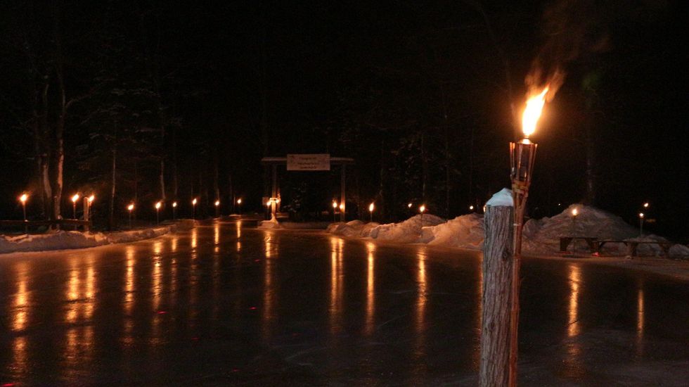 \u200bTiki torches lining a skating trail in the woods with the light reflecting on the surface.