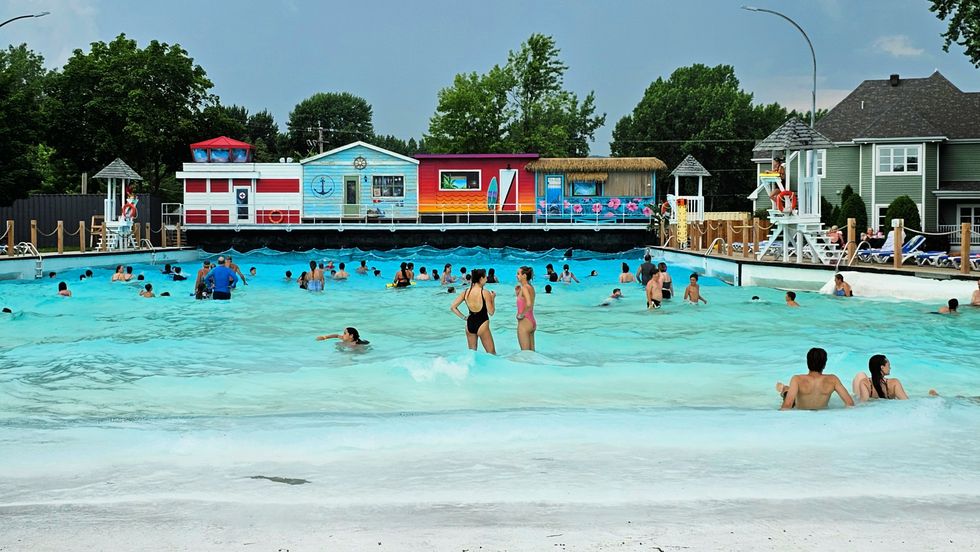 Visitors bathe in the Super Aqua Club wave pool facing multi-coloured painted beach huts.