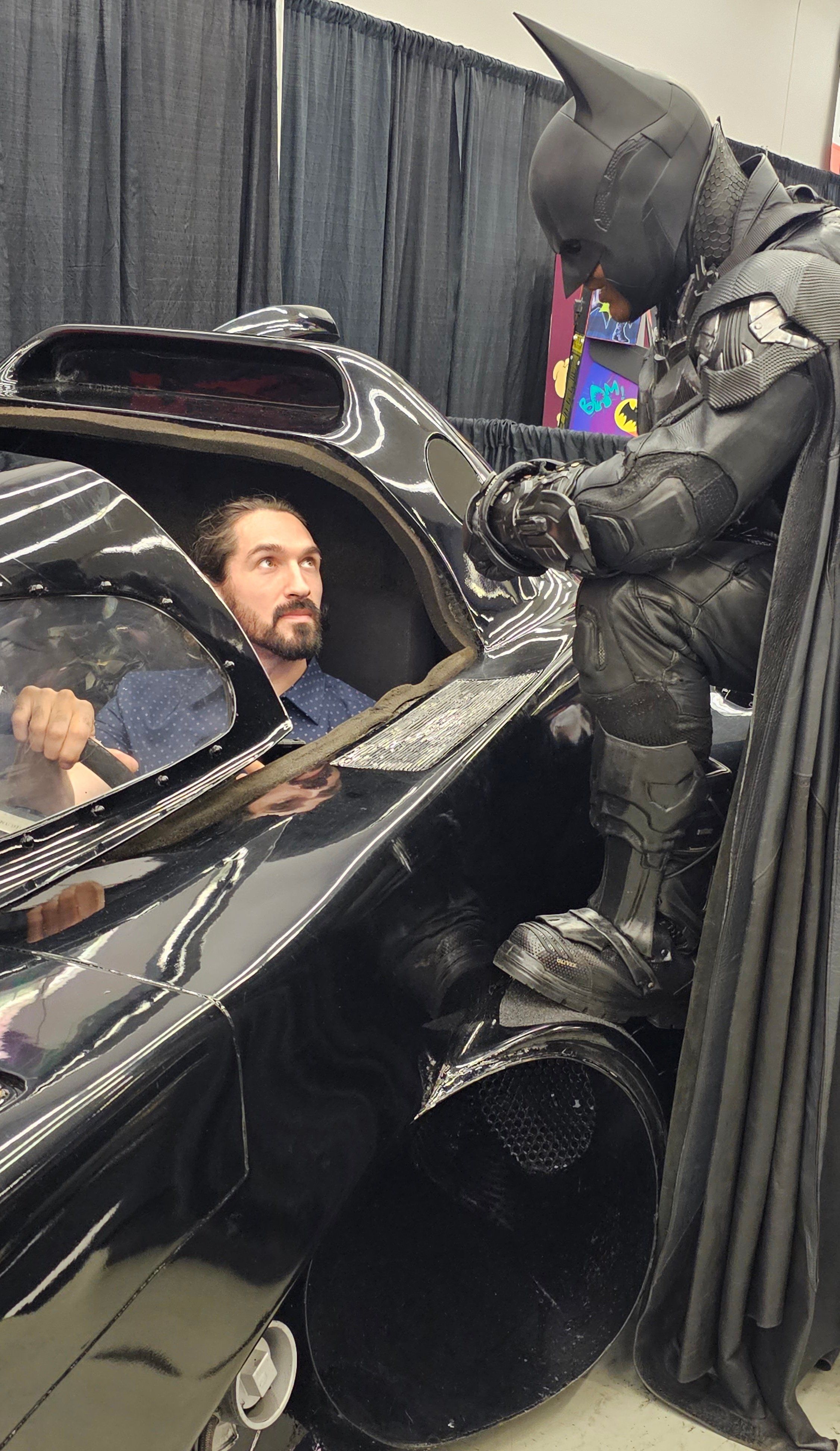 Will inside the Batmobile, while Brampton Batman leans on the car.
