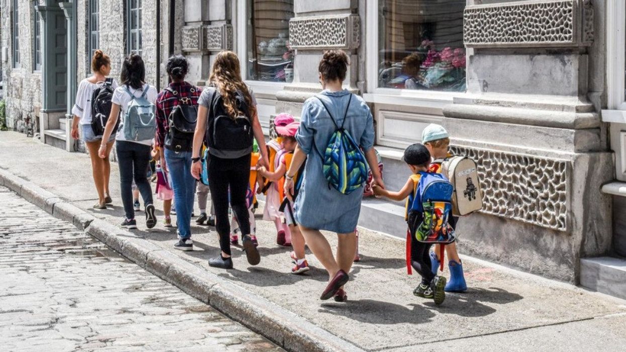 Young teachers walking small children along street. Kids wearing backpacks walking on sidewalk in romantic Montreal.